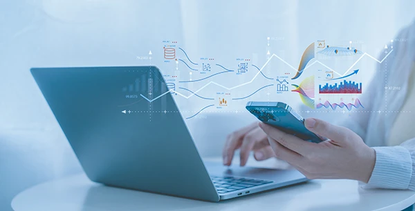 Persona usa laptop y teléfono con gráficos de datos superpuestos